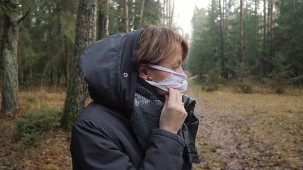 A Girl in Warm Clothes Puts on a Protective Mask in the Forest