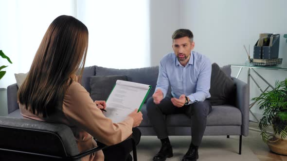 Psychologist Listens Client Taking Notes on Clipboard at Psychotherapy Session alt