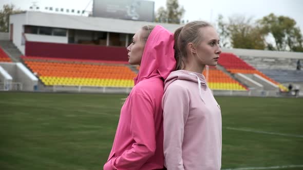 Identical Twin Sisters in Sportswear Stand Outdoor at Stadium Field Back to Back