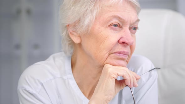 Senior wise grandmother with short grey hair holds glasses alt