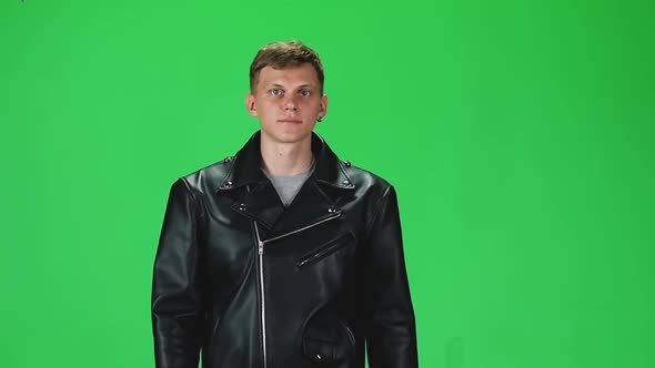 Young Man in Black Leather Jacket Going and Looking Forward Against a Green Background, Slow Motion alt