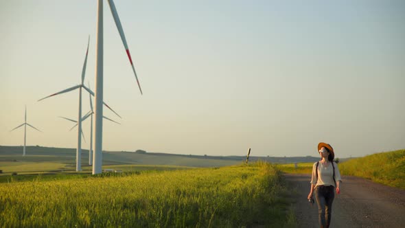 Young woman near the road with a field with alternative energy turbines alt