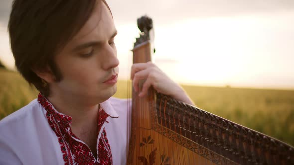 Close Up of Passionate Young Musician Kobzar Bandurist Playing on Bandura at Sunset in Wheat Field
