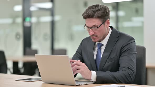 Pensive Middle Aged Businessman Thinking and Working on Laptop in Office  alt