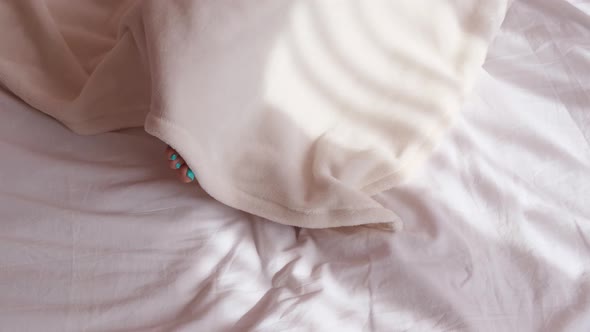 The woman is frozen in bed and covered with a blanket in the morning, women's legs top view alt