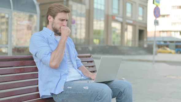 Coughing Man Using Laptop While Sitting Outdoor on Bench alt