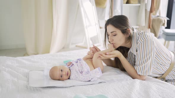 Young Woman with Long Hair Kisses Cute Little Baby Bare Leg