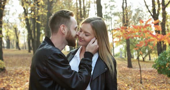 Happy Man Kisses His Cheerful Girlfriend in Sunny Autumn Park alt