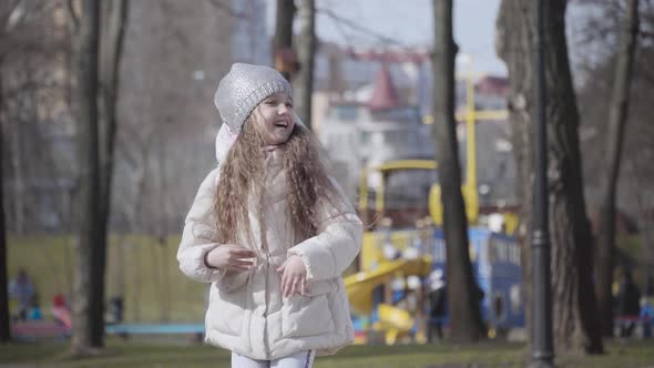 Middle Shot of Joyful Little Girl Dancing in Autumn Park. Portrait of Cheerful Pretty Child Jumping alt