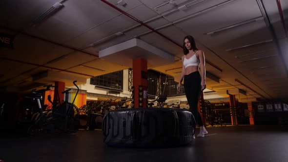 A Strong Young Woman Performs an Exercise with a Tire of a Large Tractor