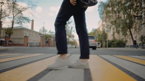 Young Man in a Blue Pants and White Sneakers Is Crossing the Road