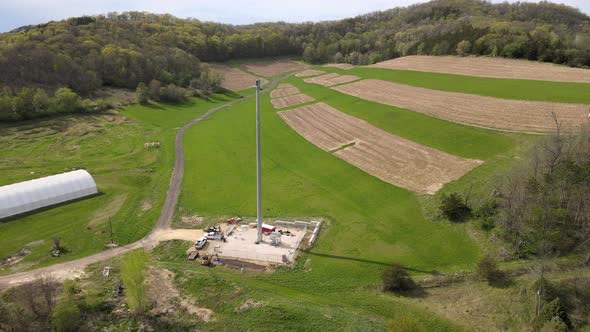 Drone view of farm field with storage and cell tower in midwest valley with forest covering bluffs.