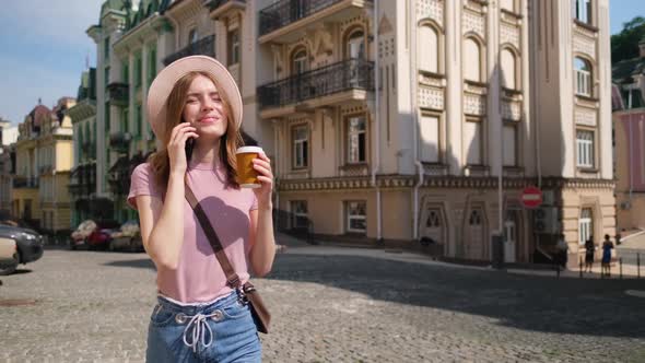 Beautiful Young Woman Tourist with Takeout Coffee in the City Center Talking on the Phone alt
