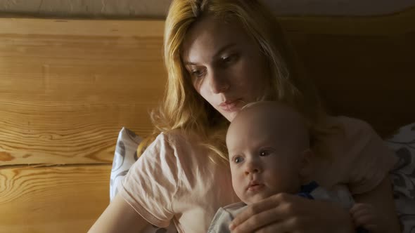 a woman with a child lies in a bed by the light of a lamp