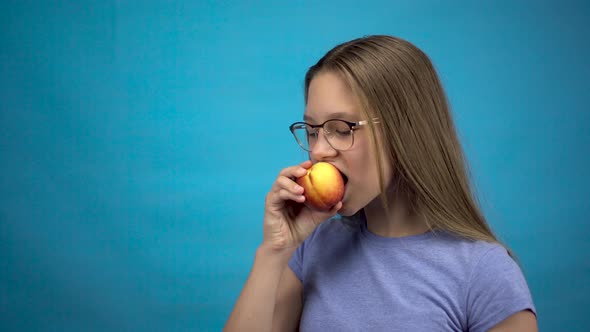 Teenager Girl with Braces on Her Teeth Eats a Peach on a Blue Background. Girl with Colored Braces alt