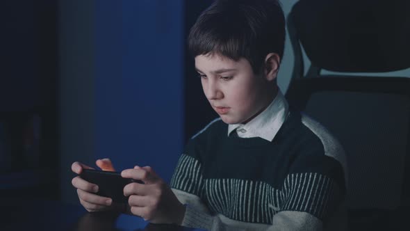 Portrait of Handsome Boy Playing Video Game with Smart Phone Indoors alt