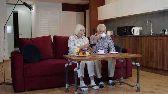 Senior Grandparents Couple Talking and Using Digital Tablet Computer at Home. Coronavirus Lockdown alt