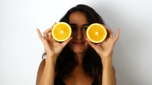 A beautiful mixed-race woman with dark hair smiling and dancing with oranges. alt