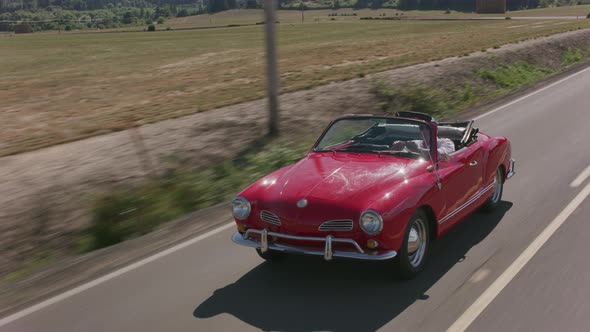 Tracking shot of man driving classic convertible car on country road.  Fully released for commercial