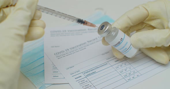 Close Up of Hand Filling a Syringe with Liquid From a Vial with a Label Reading Covid19 Vaccine alt