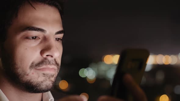 Extreme Closeup of Handsome Young Man Face Using His Smartphone at Night. With Copy Space
