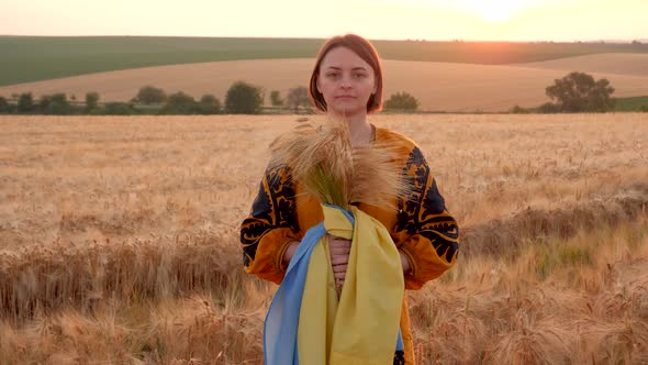a woman in an embroidered shirt in a wheat field with a blue-yellow flag of Ukraine