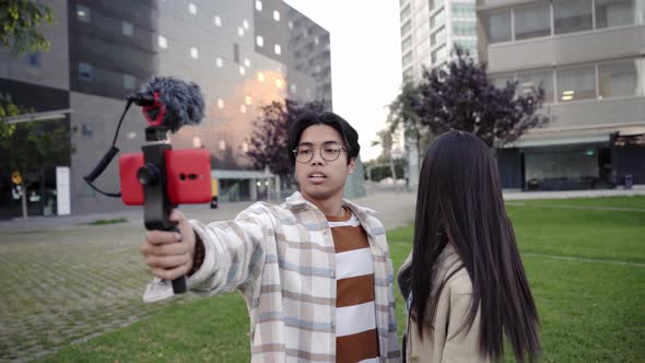 Couple of Beautiful Asian Influencers Using Smartphone to Streaming Live Video Showing the City and alt