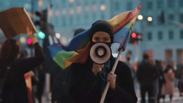 Woman with Face Mask Speaking Into the Megaphone While Holding Rainbow Flag. Demonstration Against alt