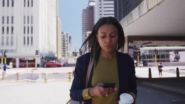 African american woman holding coffee and using smartphone in street alt