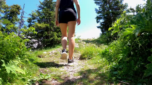 A woman walks down a rocky road in sneakers. Hiking in the mountains. alt