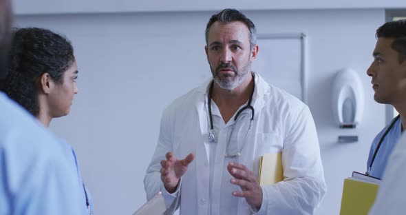 Senior caucasian male doctor discussing with diverse colleagues at a hospital staff meeting alt