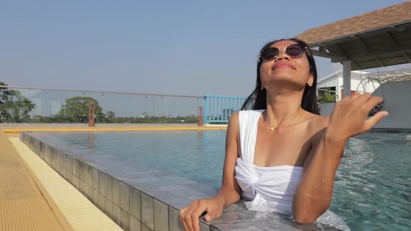 A pretty woman in white swimsuit relaxing by the poolside during summertime in Pattaya Hotel - Close alt