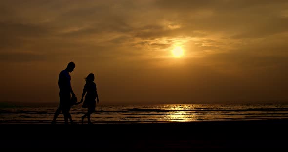 Silhouette a Family with a Baby Walking Along the Seashore at Sunset