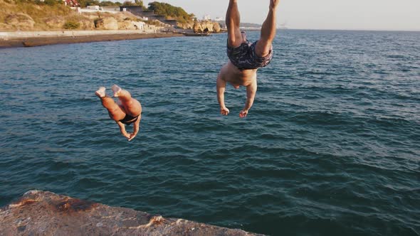 Young Woman and Man Jumping From a Pier Into the Sea During Beautiful Sunrise Super Slow Motion alt