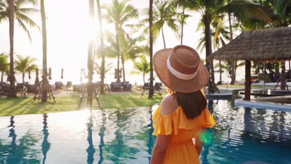 Young woman traveler relaxing and enjoying the sunset by a tropical resort pool alt