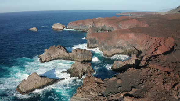 Aerial dolly of rocky coastline of harden brown lava and ocean surf alt