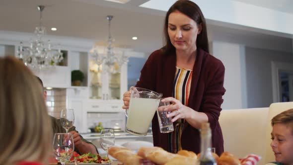 Smiling caucasian mother pouring lemonade for children at table before family meal alt