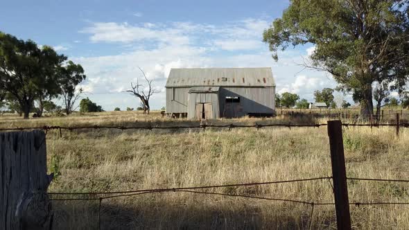 Aerial footage moving through agricultural land, past a barbed wire fence and an old barn made from alt