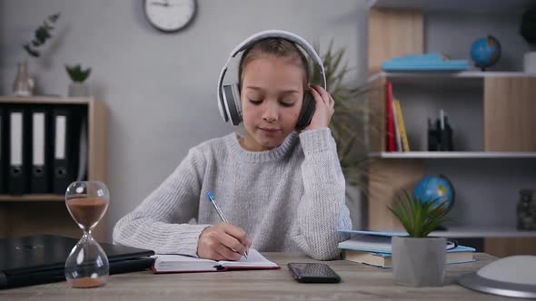 Teen Girl in Headphones which Sitting at the Table and Making Notes Into Her Diary alt