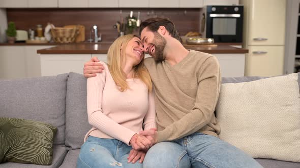 Happy Beautiful Young Wife and Husband Sitting on the Couch in Embraces alt