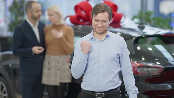 Satisfied Caucasian Car Dealer Showing Yes Gesture in Slow Motion and Smiling Looking at Camera with alt