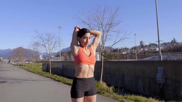 Young athletic woman stretching triceps and shoulders before outdoor workout alt