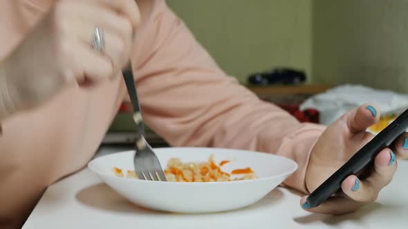 a Woman Eats Rice with a Fork and Flips Through Her Smartphone with Her Fingers alt