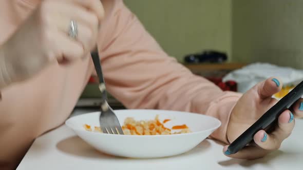 a Woman Eats Rice with a Fork and Flips Through Her Smartphone with Her Fingers