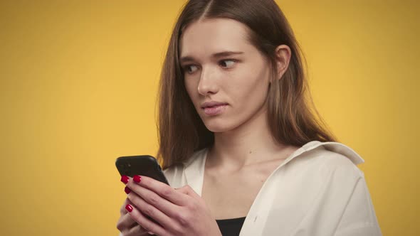 Young Adult Caucasian Woman is Thinking an Answer on Her Smart Phone on a Bright Yellow Background alt