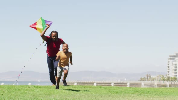 Video of happy african american father and son running, having fun with kite outdoors alt