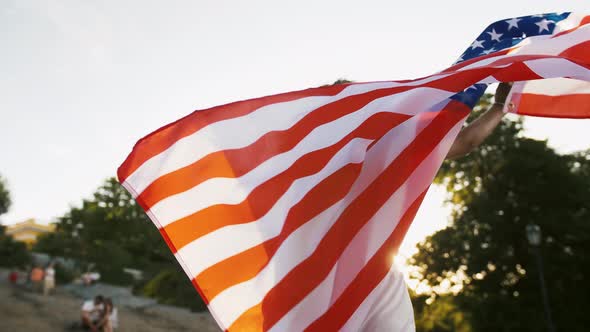 Africanamerican Woman in White Outfit and Sunglasses is Holding Flag of USA Smiling and Waving It alt