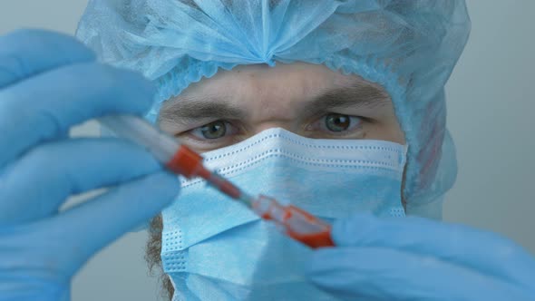 Portrait of young caucasian male doctor in medical face mask takes blood samples. alt