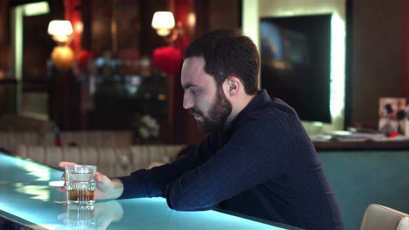 Frustrated Young Man Sitting at the Bar Counter and Holding Glass alt