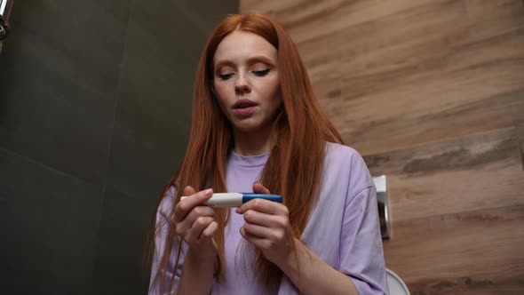 Young Caucasian Woman Hopefully Checking at Pregnancy Test and Feeling Broken Sitting on Toilet Bowl alt